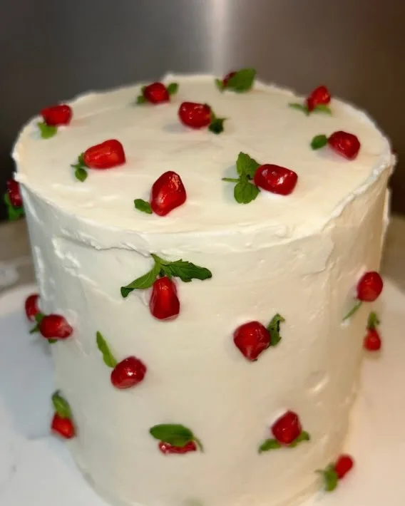 A tall white frosted cake dotted with pomegranate seeds and mint